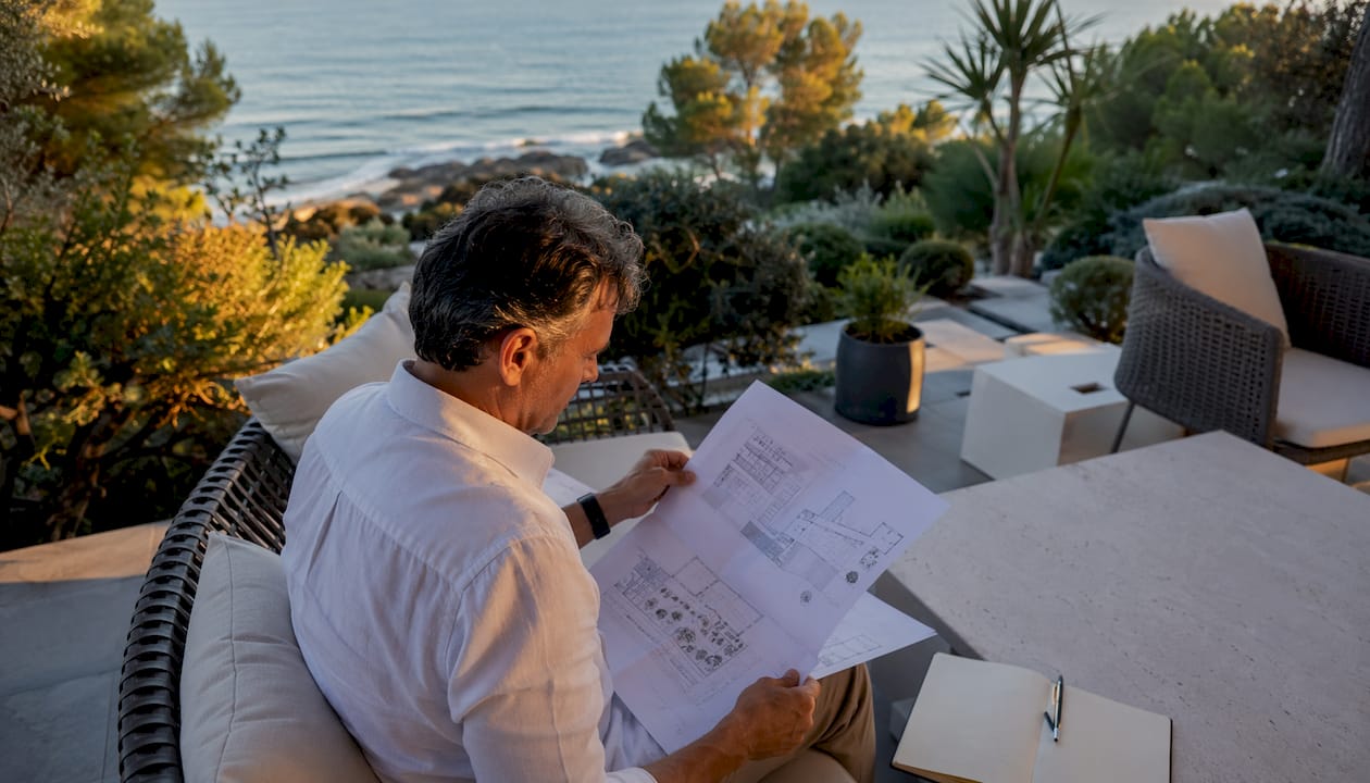 Un hombre analiza unos planos en una exclusiva villa frente al mar.